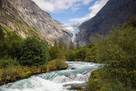 A river flows in front of the melting Kjenndalsbreen glacier between steep mountains through a