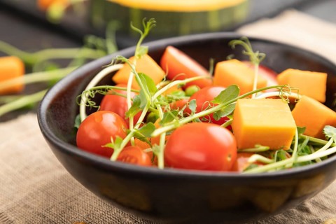 Vegetarian vegetable salad of tomatoes, pumpkin, microgreen pea sprouts on black concrete