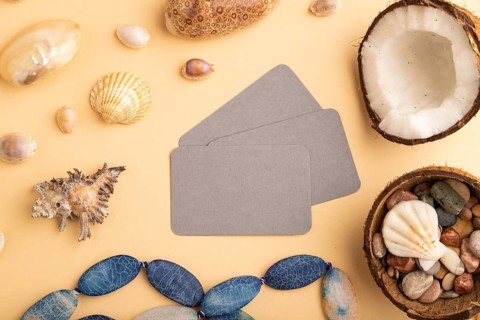 Brown paper business card with coconut, seashells, pebbles, beads on orange pastel background. Top