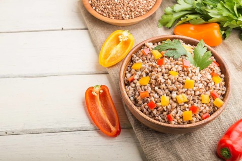 Buckwheat porridge with vegetables in wooden bowl on a white wooden background and linen textile.