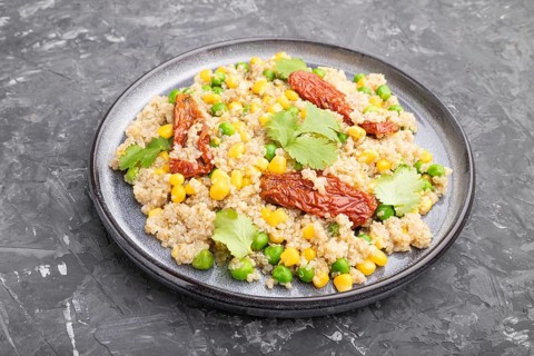 Quinoa porridge with green pea, corn and dried tomatoes on ceramic plate on a gray concrete