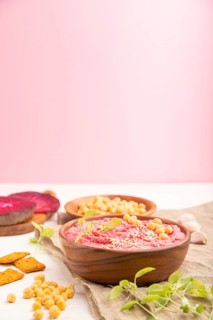 Hummus with beet and microgreen basil sprouts in wooden bowl on a white and pink background and