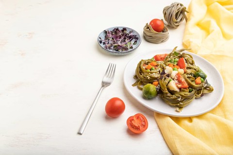Tagliatelle green spinach pasta with tomato, pea and microgreen sprouts on a white wooden