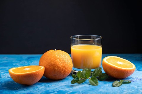 Glass of orange juice with mint on a black and blue background. Hard light, contrast. Side view,