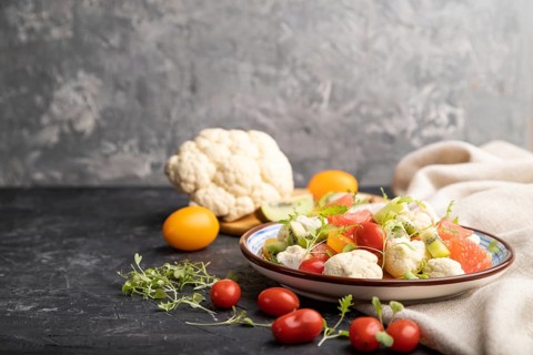 Vegetarian salad of cauliflower cabbage, kiwi, tomatoes, microgreen sprouts on black concrete