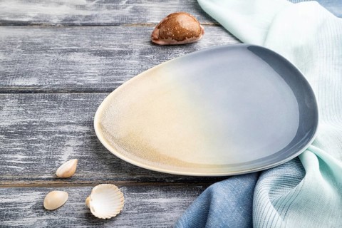Empty blue ceramic plate on gray wooden background and blue textile. Side view, close up