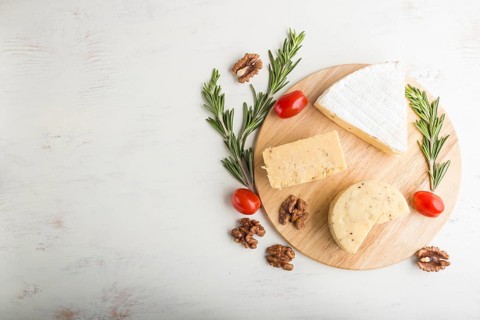 Cheddar and various types of cheese with rosemary and tomatoes on wooden board on a white wooden