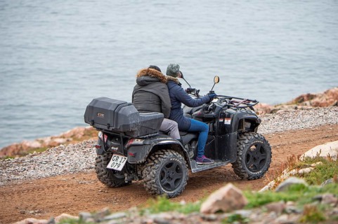 Two people ride a quad bike along a narrow gravel track near the coast, fjord, remote Arctic Inuit