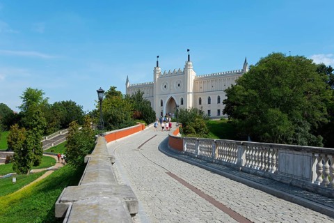 Path leads to a castle with towers and battlements, surrounded by trees and greenery, castle with