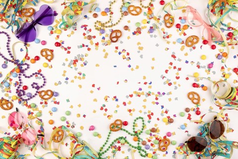 Colourful party decorations with confetti, pretzels, pearl necklaces and funny glasses on a white