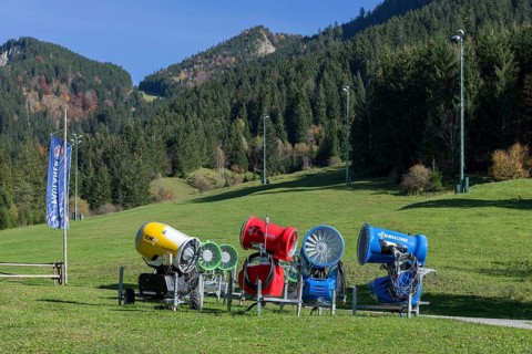 Snow cannons stand on a green meadow in front of a sunny mountain landscape, Schwangau, Ostallgäu,