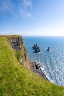 Young man standing on cliff, view from steep cliff to the rocks Reynisdrangar in the water, at