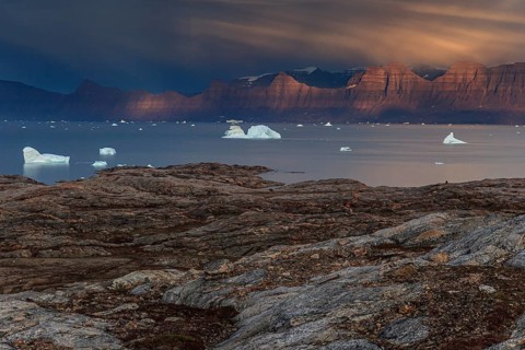 Evening light and atmosphere in fjord with icebergs in front of steep mountains, cloudy, autumn,