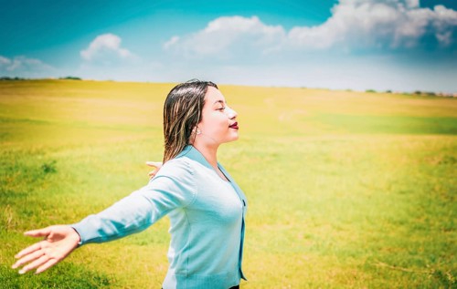 Happy girl spreading arms breathing fresh air in the field. Relaxed woman breathing fresh air in a