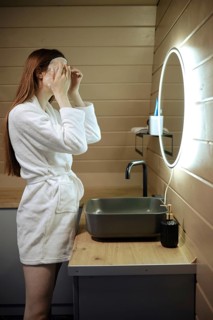 Unrecognizable woman smoothes a sheet mask on her face while standing in the bathroom in front of a