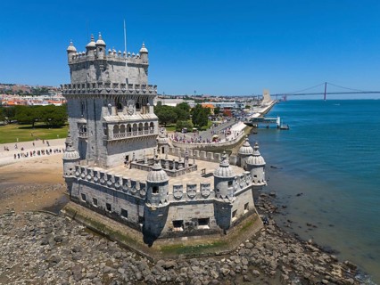 A tower on a riverbank with a bridge in the background and a clear blue sky, aerial view, Torre de