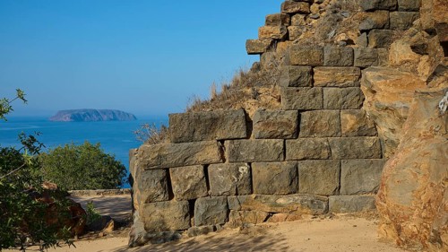 Ancient stone structures against a clear blue sky with the sea in the background, Palaiokastro,