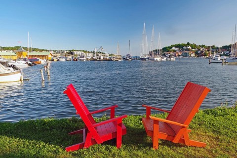 Two red wooden chairs on a lawn overlooking a sunny harbour, Sandefjord, Norway, Europe