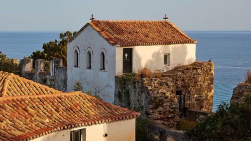 A white house with a church in the background against the sea in the evening sun, Koroni, Byzantine