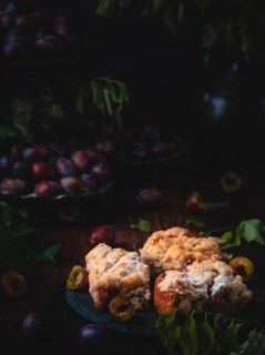 Plum cake on a plate in a dark, cosy, autumnal setting with plums and leaves
