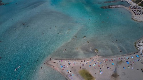 Overtourism, aerial view of a beach with many people and colourful umbrellas, surrounded by
