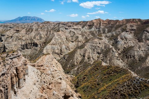 Extensive hilly desert landscape with dry vegetation and rocks under a clear blue sky, Barranco de
