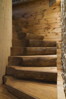 Illuminated twisting wooden staircase with brown stained half log steps attached to large bleached