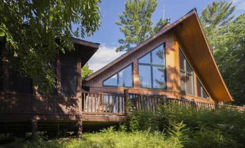 Back view of a milled cottage style flat log profile home with elevated wooden deck and landscaping
