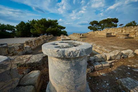 Stone column in the middle of an ancient ruins field with trees and stone structures in the