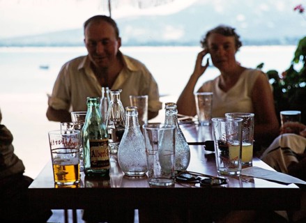 Menschen um einen Tisch mit Getränken und Flaschen in einem Hafencafé in Calvi, Korsika,