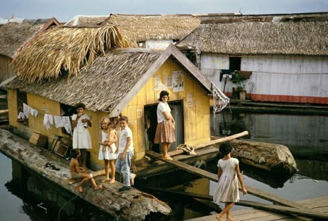 Woman and children in an informal housing area with wooden huts built on logs, known as the