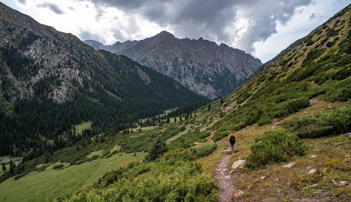 Mountaineer on hiking trail in green mountain valley with river and steep mountain peaks, Chong