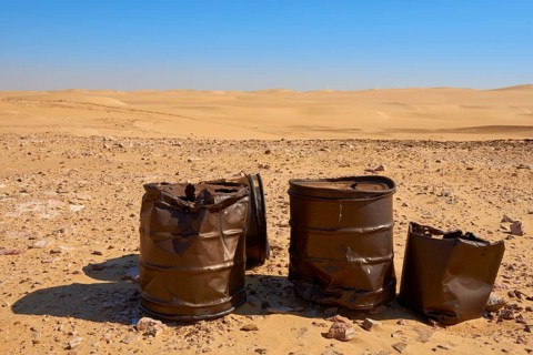 Rusty barrels stand in a vast, sandy desert landscape under a clear blue sky, Matruh, Great Sand