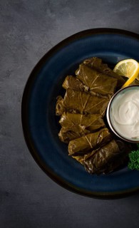 Dolma, cabbage rolls, grape leaves with filling, white sauce, lemon and herbs, rustic, selective