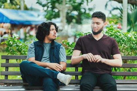 Man smoking cigarette near people in public. Man smoking and exhaling smoke to another person near