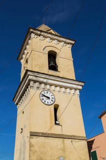 Yellow stucco cladded bell tower with white and black clock face in late summer, Manarola village,