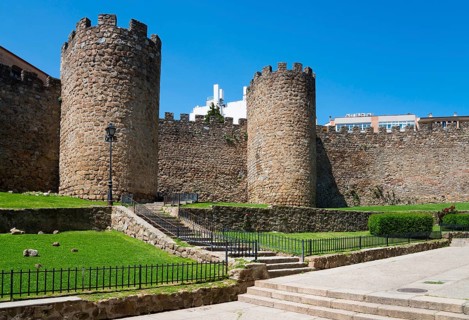 An old castle with massive stone walls and towers surrounded by greenery on a sunny day, city