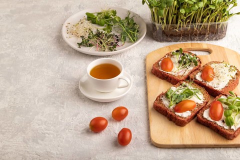 Red beet bread sandwiches with cream cheese, tomatoes and microgreen on gray concrete background.