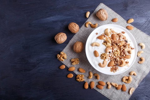 White plate with greek yogurt, granola, almond, cashew, walnuts on black wooden background. top
