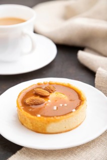 Sweet tartlets with almonds and caramel cream with cup of coffee on a black concrete background and