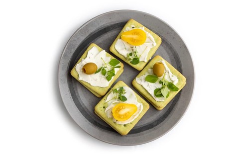 Green cracker sandwiches with cream cheese and cherry tomatoes on gray plate isolated on white