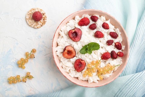 Rice flakes porridge with milk and strawberry in ceramic bowl on white concrete background and blue