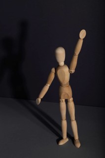 Wooden mannequin stands with raised hand on gray background. protest, attention concept. copy