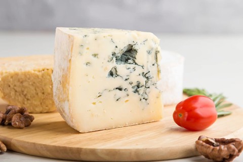 Blue cheese and various types of cheese with rosemary and tomatoes on wooden board on a white