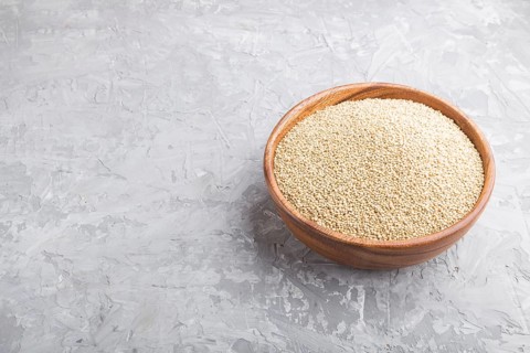 Wooden bowl with raw white quinoa seeds on a gray concrete background. Side view, close up, copy