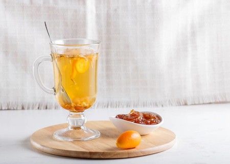 Jasmine tea with kumquat in a glass cup on a wooden board on a white background. close up, copy