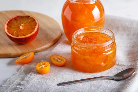 Orange and kumquat jam in a glass jar with fresh fruits on a white linen tablecloth. Homemade,