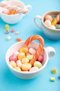 Heap of multicolored caramel candies in cups on blue pastel background. close up, side view,