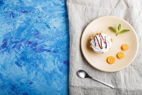 Cake with whipped egg cream on a light brown plate with kumquat slices and mint leaves on a blue