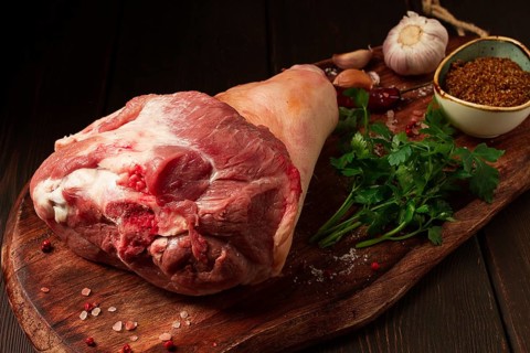 Raw pork knuckle, on a wooden chopping board, with spices, close-up, top view, no people